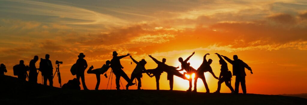 Group of people silhouetted against a vibrant sunset, showcasing unity and joy.